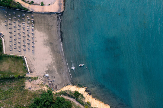 Aerial view of a sandy beach with rows of umbrellas and small boats in the turquoise sea near rocky cliffs in Zvernec, Vlore County, Albania.