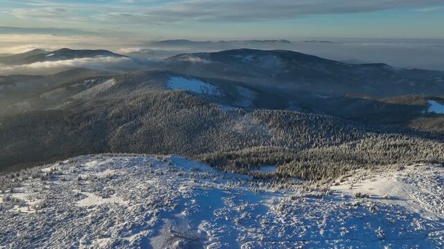Aerial orbital rotation around snowy Pilsko mountain peak at sunset with distant ranges