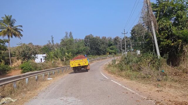 Tracking video of tractor loaded with soil moving along road in rural setting in village