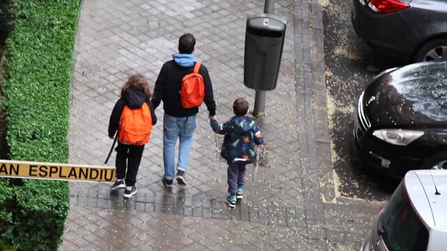 Padre llevando de la mano a hijos al colegio con mochila para estudiar infantil educaci&oacute;n