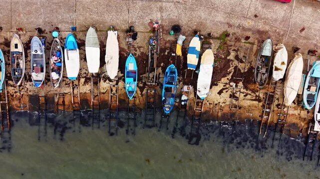 Colorful watercraft parked on wooden ramps along concrete shoreline. Top-down aerial view of fishing boats on slipways, Pomorie, Bulgaria.