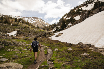 Fototapeta premium Male hiker with backpack walking along a rocky mountain trail surrounded by pine trees and alpine vegetation in the Spanish Pyrenees. Adventure travel, hiking and outdoor recreation 
