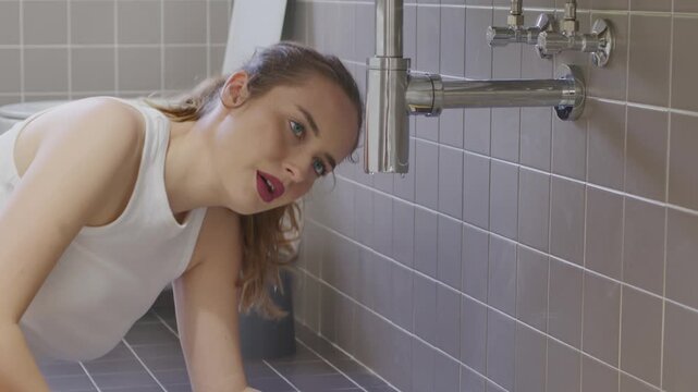 Worried young woman looking at leaking pipe under bathroom sink home emergency
