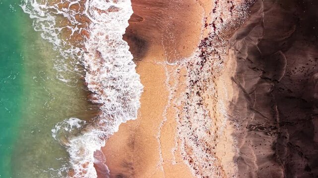 Color gradients from green water to white foam and black beach shoreline. Aerial view of ocean surf and dark sand beach.