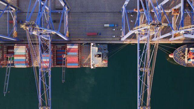 Stunning aerial top-down view of gantry cranes loading and unloading shipping containers from a large cargo vessel docked at a bustling commercial port, highlighting global trade and logistics
