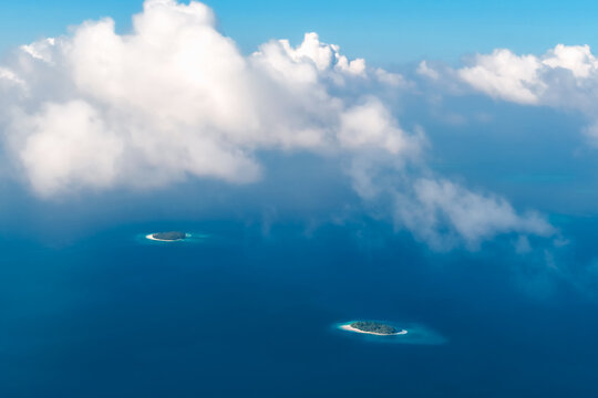 Aerial view of two small tropical islands surrounded by turquoise coral reefs and deep blue ocean water under soft white clouds Kudahuvadhoo, Dhaalu Atoll, Maldives.