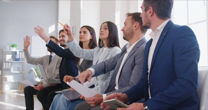 Business people group training meeting with active participation. Professionals raise hands to ask questions in an interactive strategy workshop. Men and women voting in office during a meeting. 