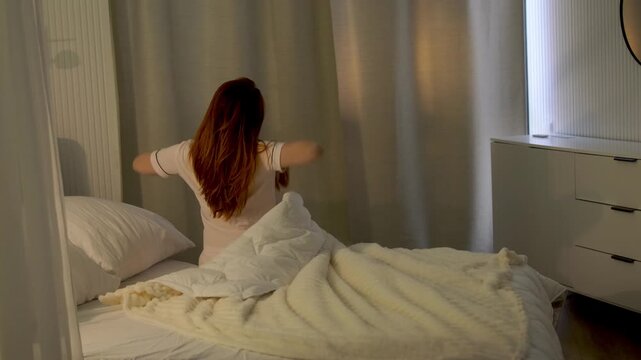 Young woman gets out of bed in a bright bedroom and begins her morning routine. Relaxed home lifestyle scene with a peaceful start to the day