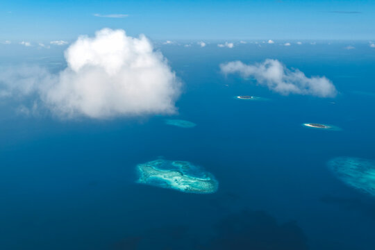 Aerial view of tropical islands and coral reefs scattered across the deep blue Indian Ocean under fluffy white clouds in Kudahuvadhoo, Dhaalu Atoll, Maldives.