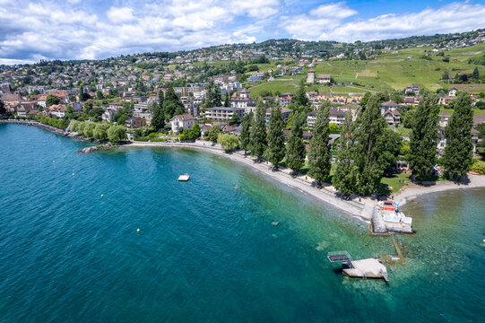 Aerial view of the town of Lutry on the shores of Lake Geneva with lush vineyards, residential houses on the hillside and tall trees by the water Lutry, Vaud, Switzerland.