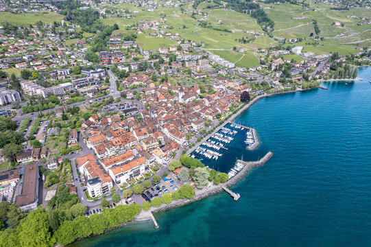 Aerial view of the historic town of Lutry with its harbor, red-roofed buildings, and lush green vineyards on the shores of Lake Geneva in Lutry, Vaud, Switzerland.