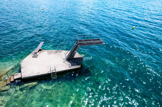 Aerial view of a concrete diving platform with metal ladders and boards in the clear turquoise water of Lake Geneva in Lutry, Vaud, Switzerland.