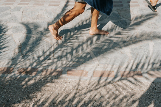 Barefoot person walking on a stone path with palm tree shadow