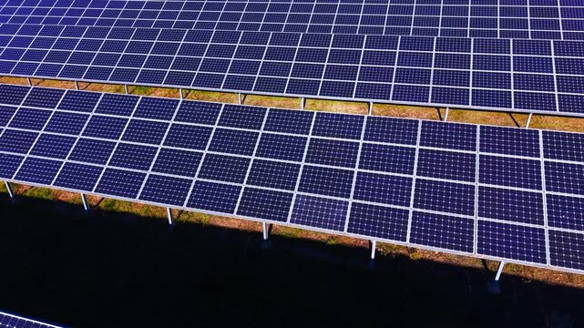 Rows of dark silicon modules casting shadows onto the soil. Industrial solar collectors mounted on metal frames.