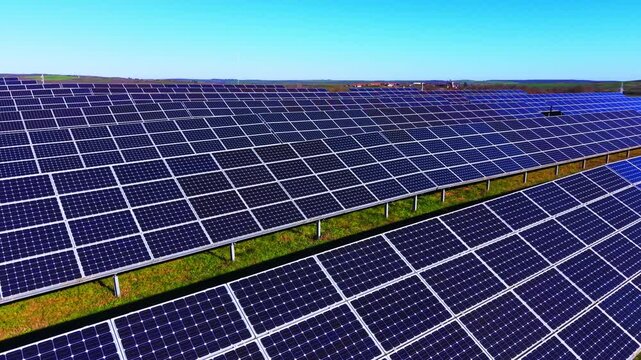 Low angle wide panoramic vista of a large clean infrastructure park generating green power. Vast array of sun tracking solar panels under blue sky.