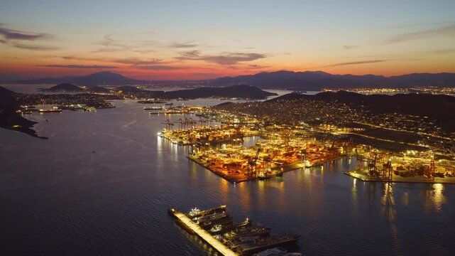 Breathtaking aerial footage capturing the port of piraeus in athens, greece, brilliantly illuminated against a spectacular twilight sky, showcasing the bustling global trade hub