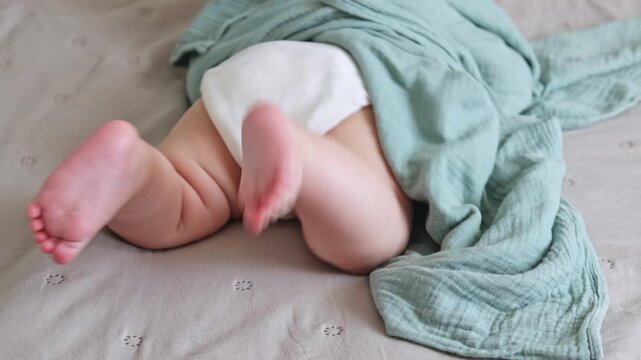 Cute baby boy learning to roll over from back to tummy on a soft bed. Sweet infant development milestone, active moving in nursery room. Early childhood, growth and parenting concept.