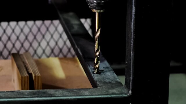 Close-up metallic twisting drill bit drilling a dark metallic surface, stained with metal shavings and lubricant. Metal processing. Construction works. Macro shot. B-roll 4K slow motion footage.