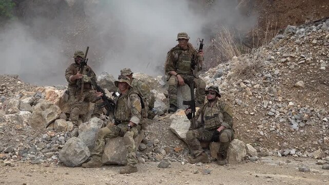 Military training exercises in a rocky area with smoke and soldiers