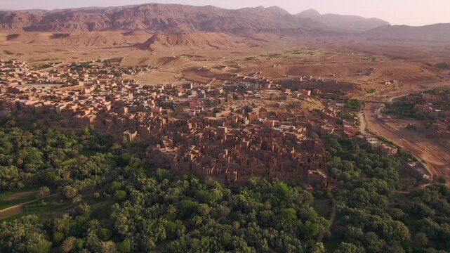 Tinghir in Draa-Tafilalet, Morocco between the High Atlas and Jbel Saghro ranges, fortified mudbrick ksar architecture emerging from Phoenix dactylifera groves and arid valley terrain parallax aerial