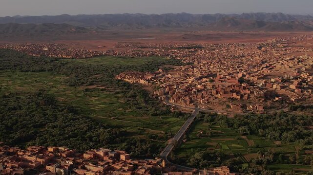 Bridge and regional roadway crossing the Tinghir valley in Draa-Tafilalet, Morocco, between the High Atlas and Jbel Saghro ranges, linking historic ksar districts with expanding urban areas, aerial