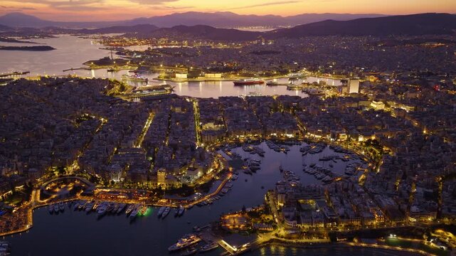 Breathtaking aerial footage capturing the illuminated city of piraeus and the bustling zea marina at twilight, showcasing the vibrant port and surrounding urban landscape against a colorful sunset