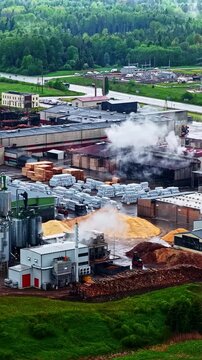 Industrial high-angle shot over the Stora Enso sawmill in Latvia. Features thick white steam venting from a factory smokestack next to large piles of processed woodchips and a green forest line.