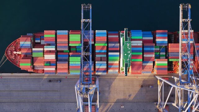 Stunning aerial top-down perspective of a massive container ship moored at a bustling port, with gantry cranes actively loading and unloading colorful cargo containers from the vessel