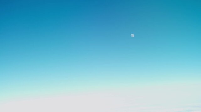 Airplane passenger window view of daytime moon and blue sky over clouds inflight, handheld