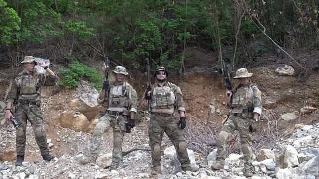 Military personnel stand at a training site with weapons in hand during a daylight exercise