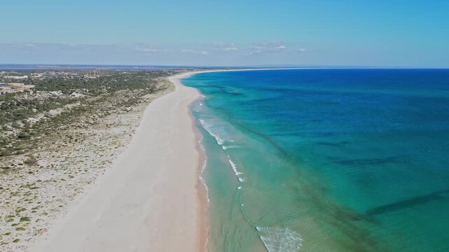 Aerial view moving along a deserted sandy beach with turquoise ocean in sunlight