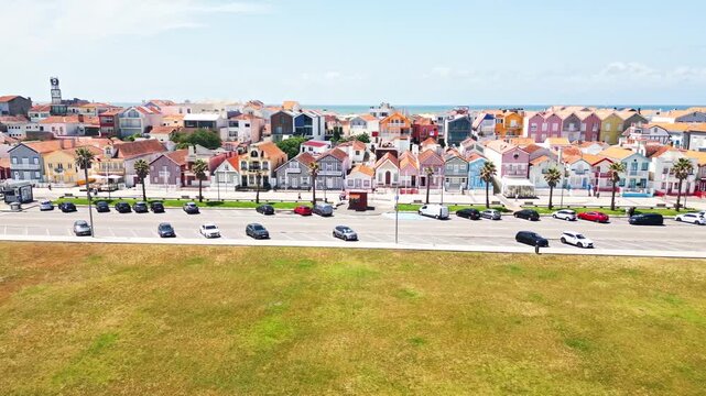 Aerial view moves toward colorful striped houses and a busy coastal street in Aveiro