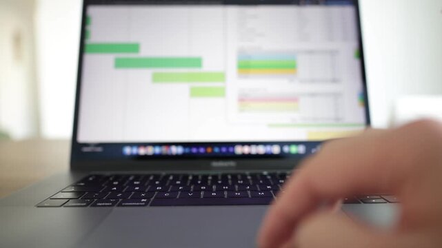 Close-up view of a laptop displaying a business analytics dashboard with statistics, pie charts, and performance data. Hands type on the keyboard while using the mouse to click and scrolling.