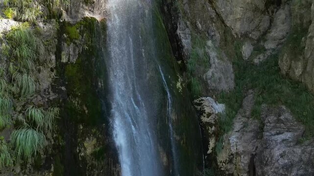Close aerial drone footage ascending beside Grunas Waterfall in Theth National Park, Albania. Captures the powerful cascade, moss-covered cliffs, and crystal-clear mountain water of the Albanian Alps.