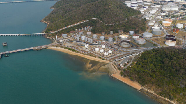 Aerial view of the Bangchak Sriracha Refinery featuring large storage tanks and industrial infrastructure along the coast near lush hills in Si Racha District, Chon Buri, Thailand.