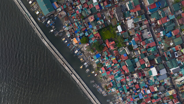 Aerial view of a dense informal settlement with colorful rooftops and small fishing boats along the coast in Manila, Metro Manila, Philippines.