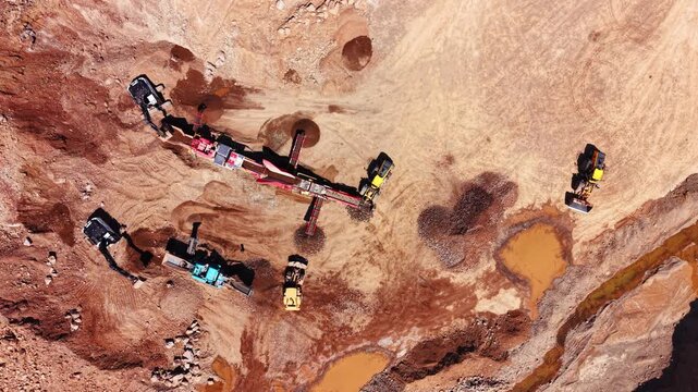 Overhead view of multiple hydraulic diggers working around a mobile sorting screener on rocky excavation ground. Excavators and crushing machinery inside stone quarry.