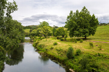 Obraz premium Calm Ohinemuri River Flowing Through Rural New Zealand Countryside