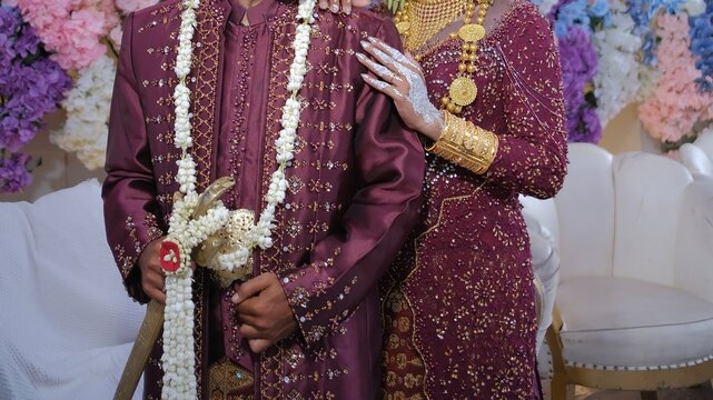 Detail of Indonesian traditional wedding dress featuring a groom holding a keris and a bride with white henna art