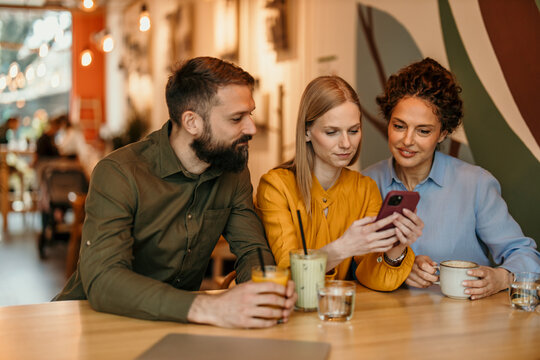 Friends sharing content on smartphone in coffee shop