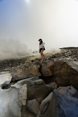 Obraz premium Hiker walking across steaming volcanic crater, Galapagos Islands. Full body side view on jagged lava boulders with dense sulfur fog behind.