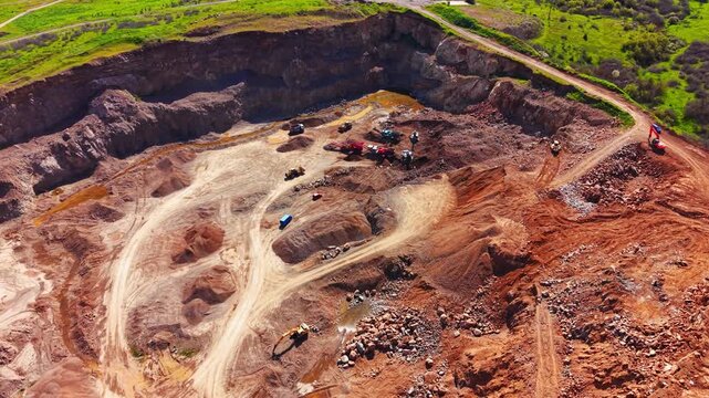 Deep excavation layers, dirt tracks, mining equipment and loose stone mounds. High angle view of deep open pit rock quarry, Bulgaria.