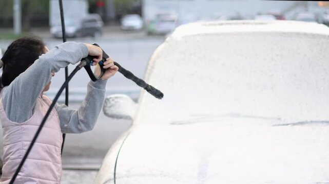 This video captures the moment a woman apply washing foam to wash her car at a self-service station. The rhythmic motion of the sponge and spray brings life to the joy of car care on a sunny day.