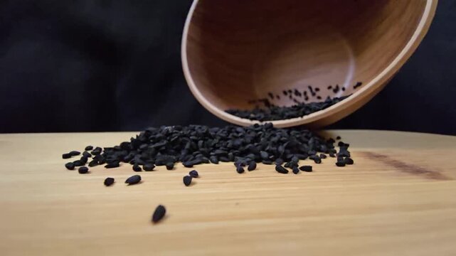 Macro shot of black seed, also known as nigella sativa or kalonji, spilling from a wooden bowl, perfect for herbal medicine and healthy food concepts.