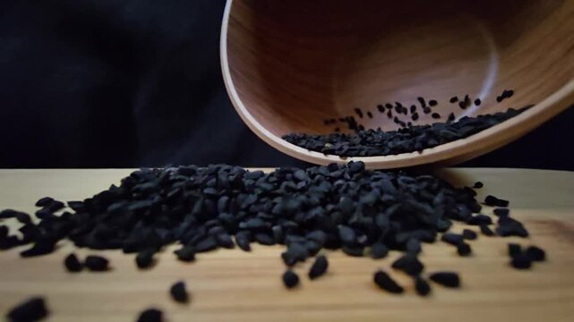 Macro shot of black seed, also known as nigella sativa or kalonji, spilling from a wooden bowl, perfect for herbal medicine and healthy food concepts.