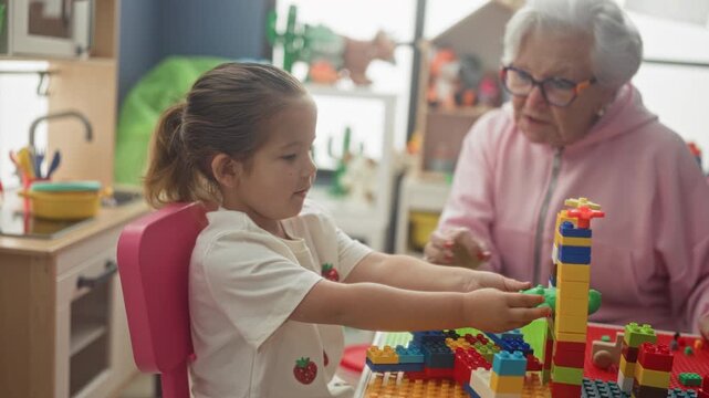 Woman placing blocks with hands while child watches in playroom; intergenerational bonding tenderness.