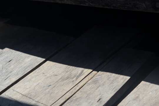 Natural sunlight casting a strong diagonal shadow across weathered wooden planks, highlighting the texture and grain of aged wood.