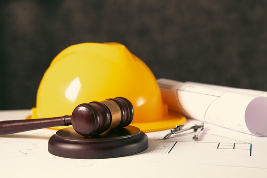 Wooden judge gavel, blueprints and hard hat on table
