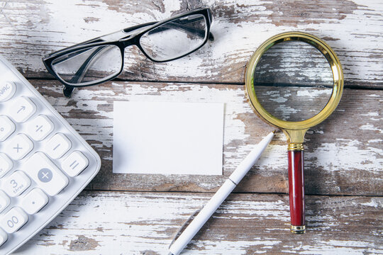 Business still life with magnifying glass, calculator, eyeglasses and blank business card