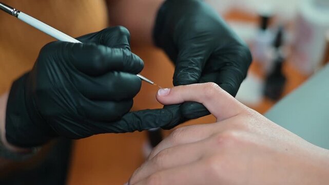 A person receives a detailed nail art design while seated in a stylish indoor environment. The artist uses a fine tool to create intricate patterns on the client's nails